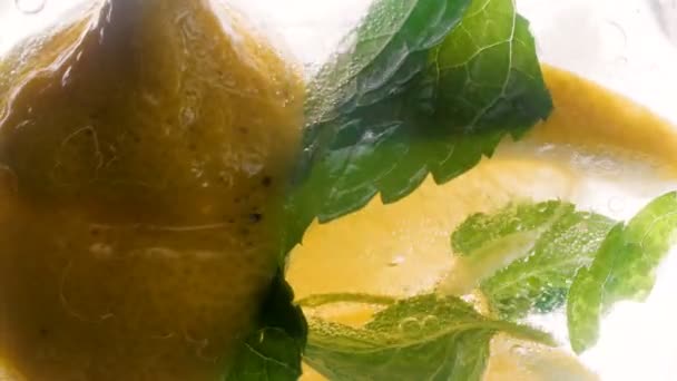 4k filmato di fette di limone, cubetti di ghiaccio e foglie di menta mescolate in vetro di limonata — Video Stock