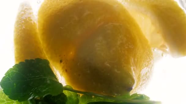Closeup 4k πλάνα του φέτες λεμόνι και δυόσμο φύλλα επιπλέει στο φρέσκο κρύα λεμονάδα — Αρχείο Βίντεο