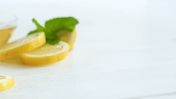 Camera panning along lemons, leaves of mint and jar with bee honey on white wooden table — Stock Video