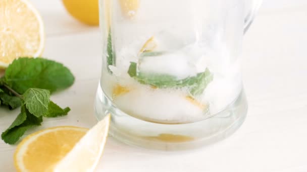 Slow motion footage of pouring carbonated water in glass with ice, lemons and mint leaves. Preparing lemonade — Stock Video