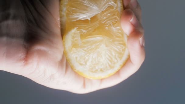 Closeup slow motion footage of hand squeezing juicy lemon against dark background — Stock Video