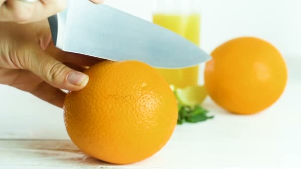 Nahaufnahme in Zeitlupe: Frau schneidet mit großem Messer Orange in zwei Hälften auf weißem Holztisch — Stockvideo