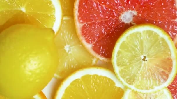 Closeup slow motion footage of fresh lemon falling on orange and grapefruit slices on table — Stock Video