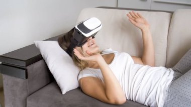 Koltukta yalan ve sanal gerçeklik kulaklık kullanarak mutlu genç kadın