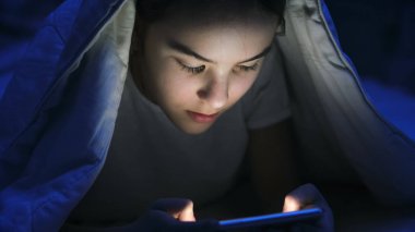 Geceleri battaniye altında smartphone üzerinde Internet tarama pijamalı kız portre fotoğrafı