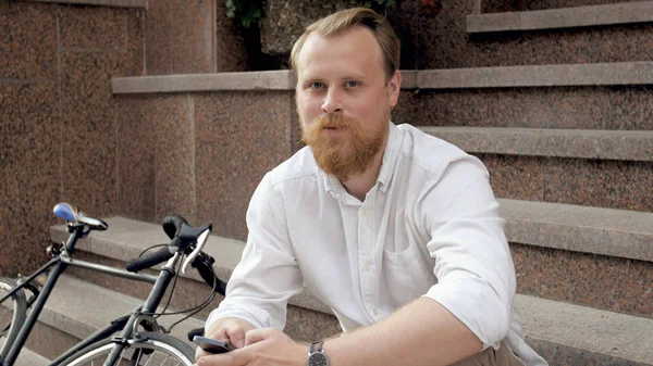 Portrait of young man with red beard relaxing on stone stairs — Stock Photo, Image