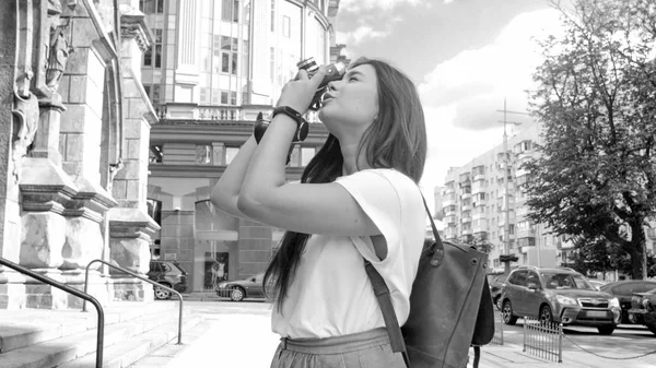 Black and white photo of stylish girl making photos on street with vintage camera — Stock Photo, Image