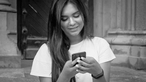 Black and white portrait of beautiful smiling woman using mobile phone on street — Stock Photo, Image