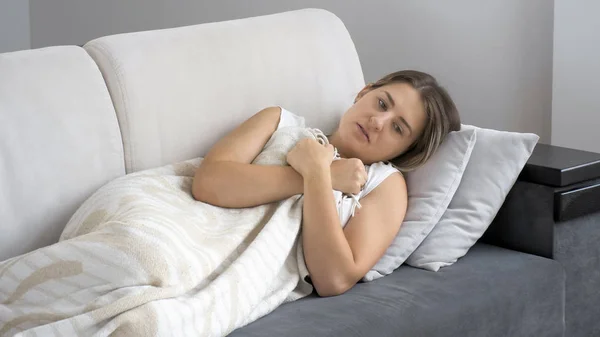 Mladá nemocná bruneta žena pocit chladu vleže pod dekou na pohovce — Stock fotografie