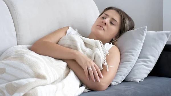 Retrato de mulher morena doente deitada sob cobertor no sofá — Fotografia de Stock