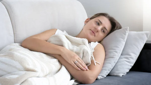 Retrato de mulher jovem com depressão deitada no sofá sob cobertor — Fotografia de Stock