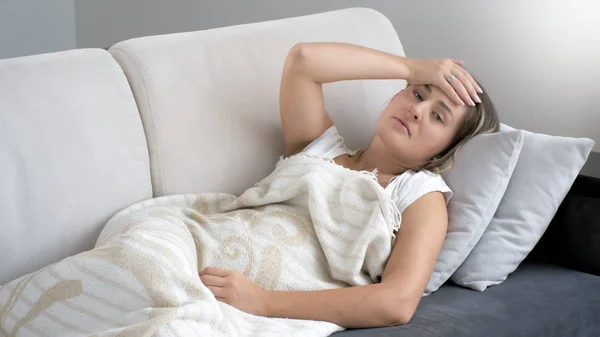 Retrato de una mujer joven acostada en un sofá y sintiéndose a alta temperatura —  Fotos de Stock