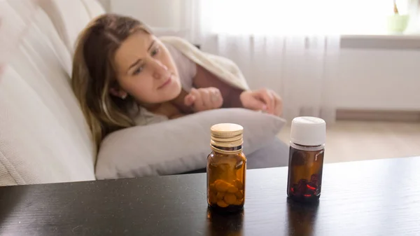 Porträtt av ung kvinna som tittar piller på sängbord — Stockfoto