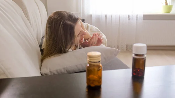 Foto de pílulas na mesa de cabeceira ao lado da mulher doente deitada no sofá — Fotografia de Stock