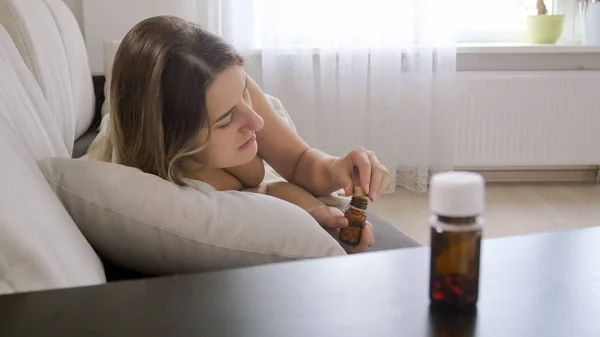 Foto de primer plano de una joven enferma acostada en un sofá y tomando pastillas —  Fotos de Stock