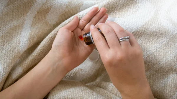 Крупный план молодой женщины, наливающей таблетки из бутылки на руку — стоковое фото
