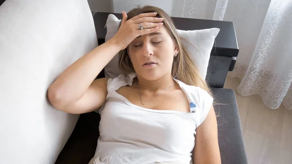 Portrait de femme malade avec froid couché sur le canapé et mesurant la température — Photo