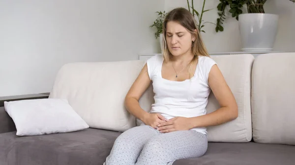 Jeune femme avec douleurs menstruelles assis sur le canapé dans le salon — Photo