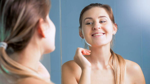 Портрет красивой улыбающейся женщины, смотрящей в зеркало в ванной комнате
