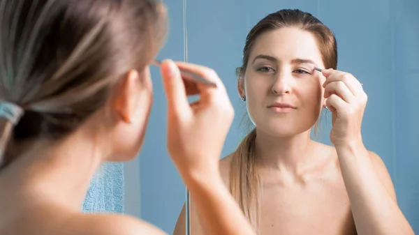 Vacker ung kvinna plockning ögonbrynen på spegel — Stockfoto