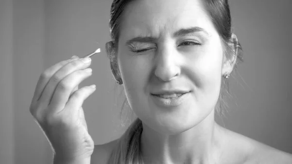 Retrato en blanco y negro de una mujer joven sintiendo dolor después de arrancar las cejas en el espejo —  Fotos de Stock