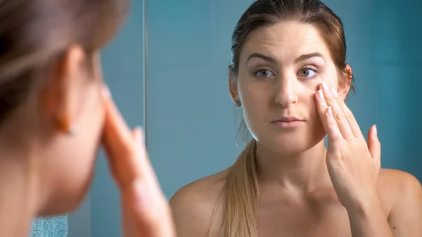 Portrait of young brunette woman looking at wrinkles in mirror — Stock Photo, Image