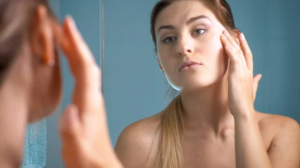 Foto da jovem mulher olhando para a pele do rosto no espelho — Fotografia de Stock