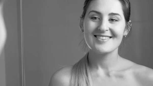 Black and white portrait of beautiful smiling woman looking at her reflection in bathroom — Stock Photo, Image