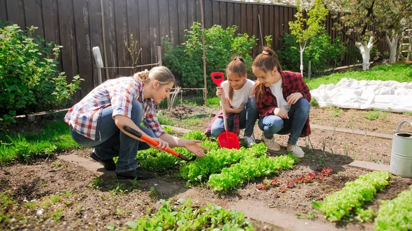 Foto de madre joven con dos niñas trabajando en el jardín — Foto de Stock