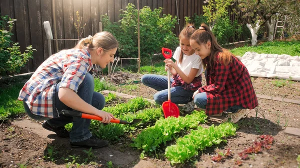 Wanita muda cantik menggali dan menanam di kebun dengan anak-anaknya — Stok Foto