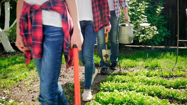Foto de primer plano de la familia sosteniendo herramientas de jardinería caminando en el jardín del patio trasero —  Fotos de Stock