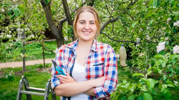 Porträt einer lächelnden jungen Frau mit Gartenscheren, die im Apfelgarten posiert — Stockfoto