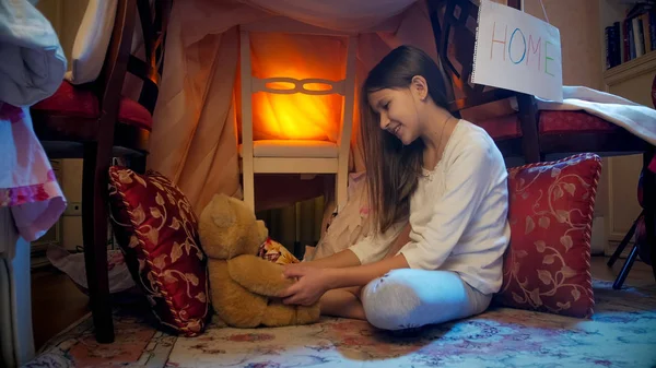 Cute little girl playing with teddy bear in tepee tent at night — Stock Photo, Image