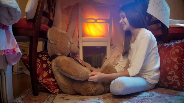 Красивая улыбающаяся девушка сидит в одеяле и играет с плюшевым мишкой — стоковое фото