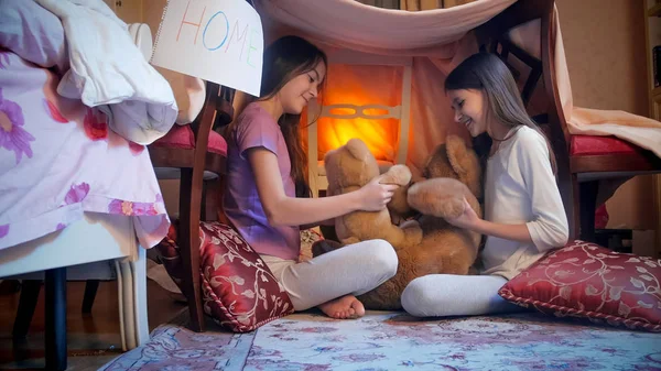 Две веселые девушки играют с плюшевыми мишками в спальне ночью — стоковое фото