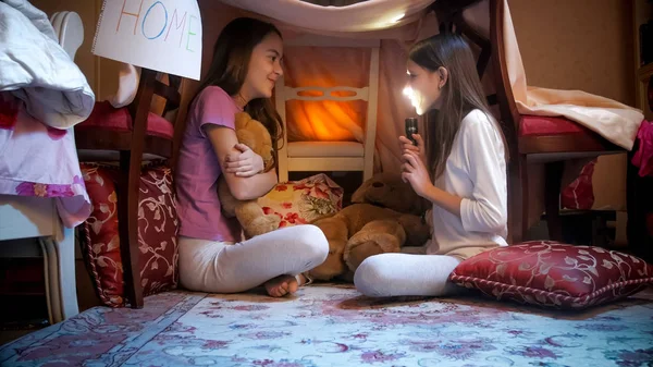 Duas meninas bonitos em pijama sentado na tenda tepee e contando histórias assustadoras — Fotografia de Stock