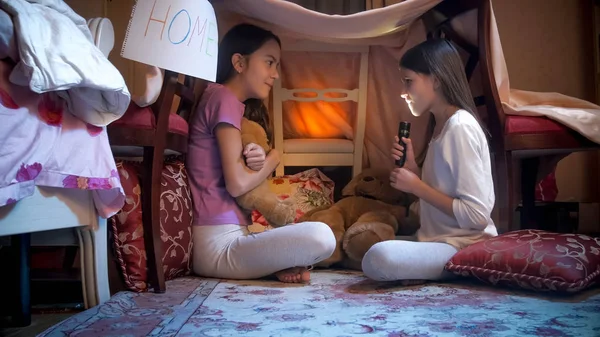 Две девушки в пижаме рассказывают истории с фонариком в самодельной палатке — стоковое фото