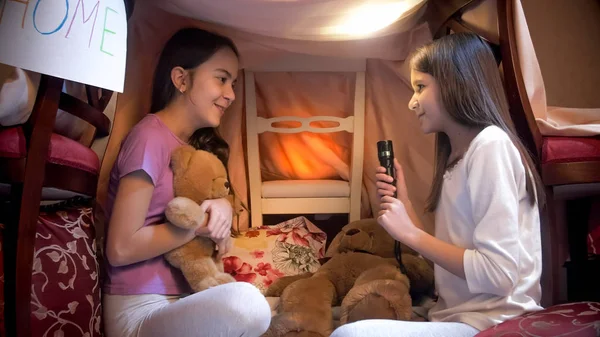 Portrait of two sisters in pajamas telling stories with flashlight at night — Stock Photo, Image