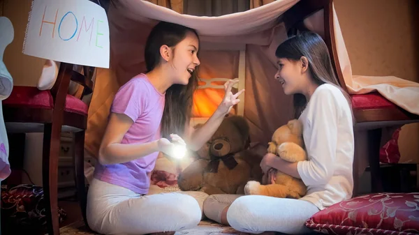 Две улыбающиеся девушки играют в палатке вигвама в спальне и рассказывают истории. — стоковое фото