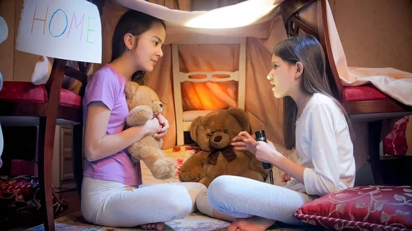 Two sisters sitting in selfmade tepee tent in bedroom and telling scary stories — Stock Photo, Image