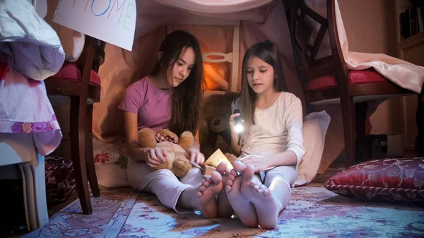 Duas adolescentes de pijama sentadas no chão no quarto e lendo livro à noite — Fotografia de Stock