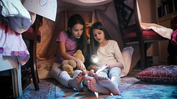 Две девушки сидят на полу ночью и читают страшную книгу — стоковое фото