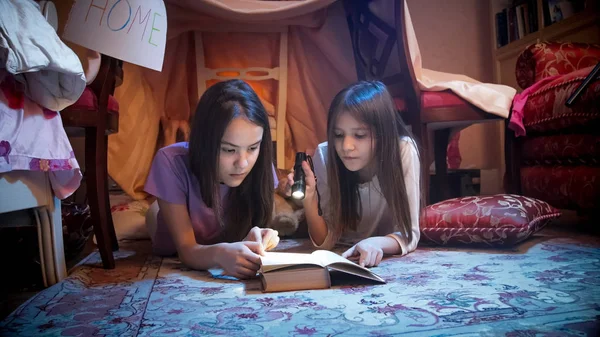 Portrait of two teenage girls reading book in bedroom at night — Stock Photo, Image