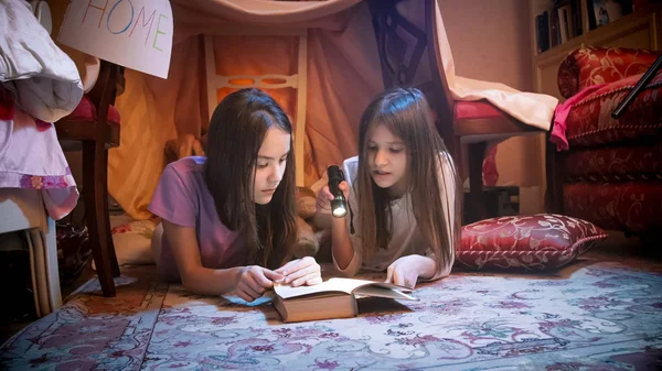 Portrait de deux adolescentes lisant un livre avec lampe de poche la nuit — Photo