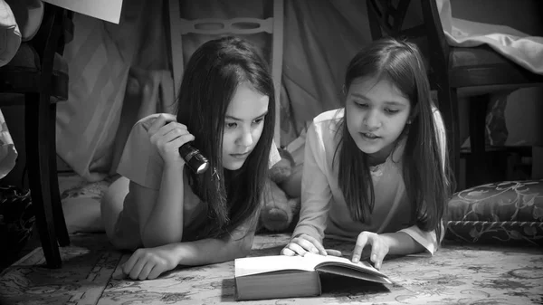 两个十几岁的女孩躺在地板上, 用手电筒看书的黑白肖像 — 图库照片