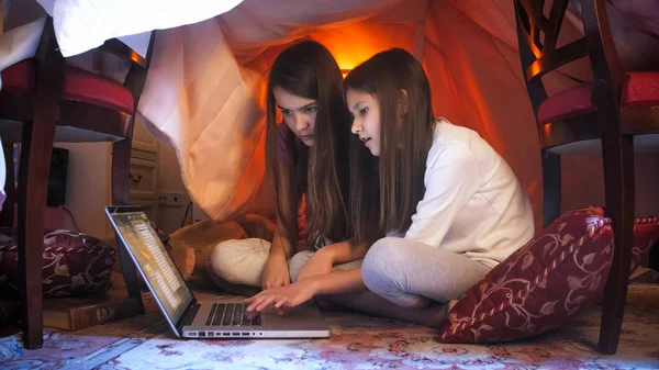 Portret dwóch sióstr w piżamie grać na laptopie w namiocie Tipi w sypialni — Zdjęcie stockowe