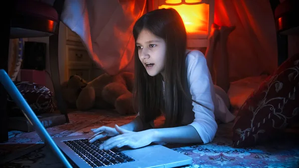 Retrato de adolescente deitada no chão no quarto à noite e usando laptop — Fotografia de Stock