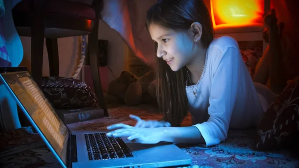 Porträtt av leende flicka i pyjamas att skriva på laptop på natten — Stockfoto