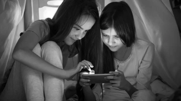 Foto en blanco y negro de dos adolescentes jugando en el teléfono móvil por la noche — Foto de Stock