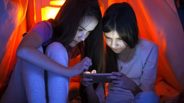 Retrato de dos niñas con teléfono inteligente en tienda de campaña tipi en el dormitorio — Foto de Stock